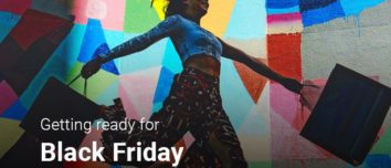 Young female with a black shopping bag with purchases in each hand, displaying happiness.